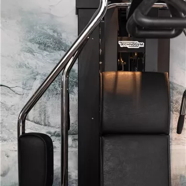 A fitness device with an adjustable bench and handles. The equipment is positioned in front of a neutral wall.