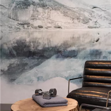 A stylish living atmosphere with a rustic wooden table and a modern armchair. In the background, there is a calming wall design featuring a landscape motif.