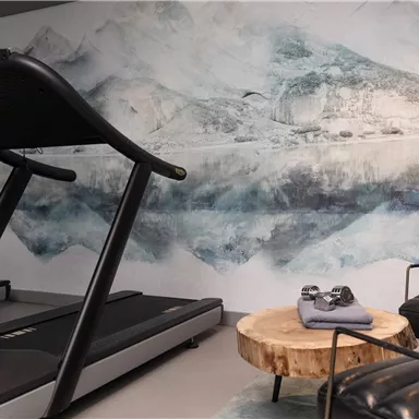 A modern gym with treadmills and a stylish wooden coffee area. In the background, there is an artistic wall design with soothing colors.