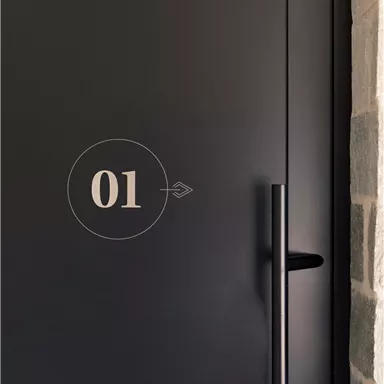 A modern black door with the number 01. The door has a minimalist handle and is surrounded by a stone wall.