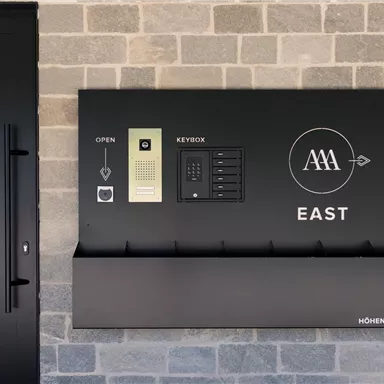 A modern entrance area with a black wall system. It includes a key box and a graphic design featuring the inscription "EAST".