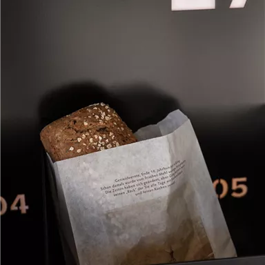 A delicious roll in a paper packaging. In the background, black walls with white writings are visible.