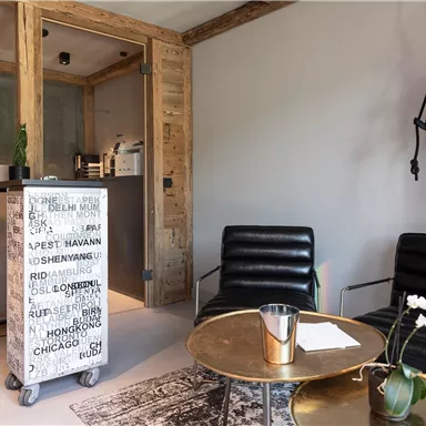 A modern waiting room with black leather chairs and a round table. The walls are made of wood, and a creative decoration featuring a monkey is visible.