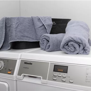 A modern washing machine with towels on it. In a clean and tidy laundry room.