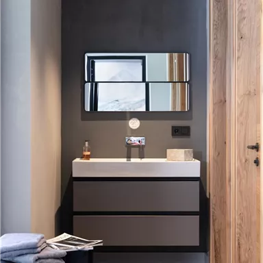 A modern bathroom with a minimalist vanity and large mirrors. The walls are in neutral tones, and there are wooden details.