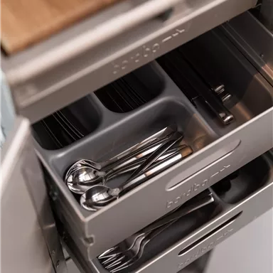 A modern kitchen drawer with cutlery and inserts. The drawer is tidy and well-organized.