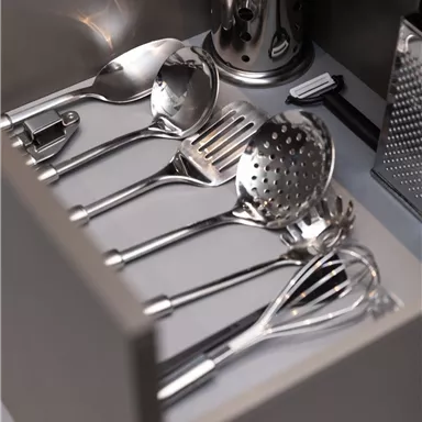 A kitchen drawer with various stainless steel utensils. Visible are spoons, a ladle, and a grater.