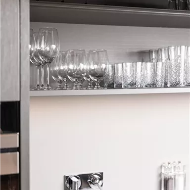 A modern kitchen cabinet with glasses and a faucet. The shelves are neatly and cleanly organized.