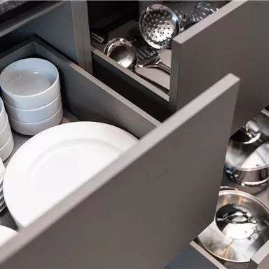 Two kitchen drawers with white plates and bowls. In the lower drawer, stainless steel pots and kitchen appliances are visible.