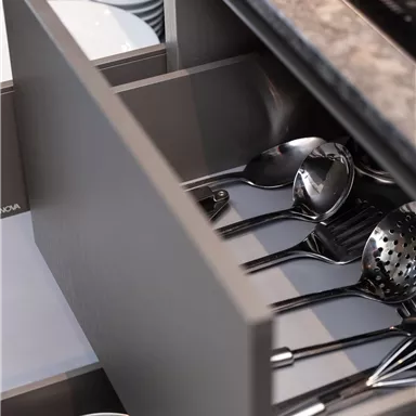 An open drawer in a modern kitchen with cutlery and cooking utensils. The drawer also contains some plates.
