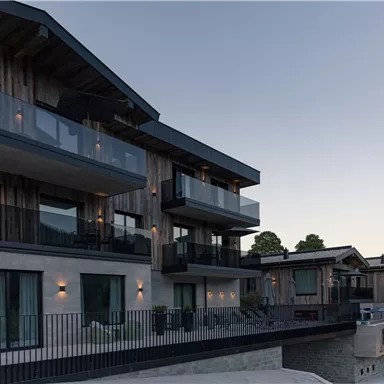 Modern holiday apartments with balconies and wooden cladding. The buildings are located in a picturesque setting and offer a beautiful view.