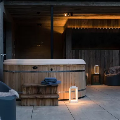 An elegant outdoor wooden hot tub in a cozy ambiance. Soft lighting and stylish furniture create a relaxing atmosphere.