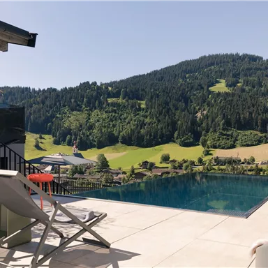 A beautiful outdoor area with an infinity pool and a view of green mountains. Relaxed loungers and a sunny atmosphere invite you to linger.