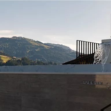 A spa area with a waterfall and a view of the hills. In the background, there are mountains and a blue sky.