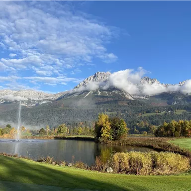 A picturesque mountain landscape with a tranquil pond. In the background, the majestic mountains and a clear sky can be seen.