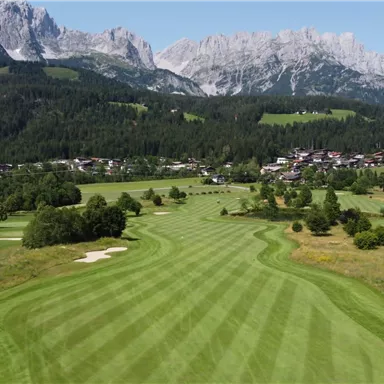 A spacious golf course with well-maintained fairways and a view of impressive mountains. In the background, a small village is visible amidst nature.