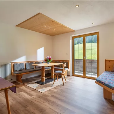 A bright and modern living room with a dining area and a cozy sofa bed. Large windows offer a beautiful view of nature.