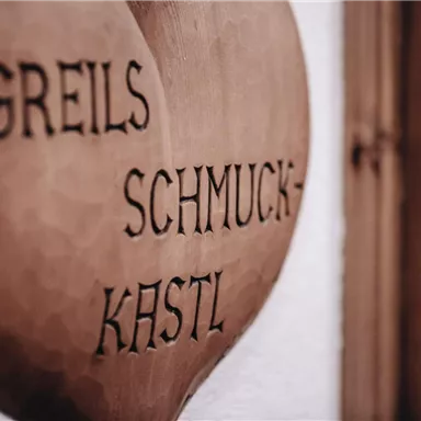 A wooden sign with the inscription "Greil's Jewelry Box". The sign has a heart-shaped form and features a rustic font.