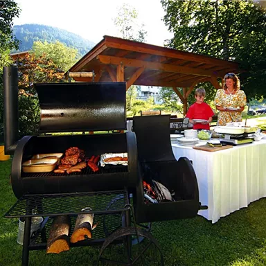 A cozy outdoor barbecue party with a grill where various types of meat are being prepared. In the background are two people preparing the food, surrounded by lots of greenery.