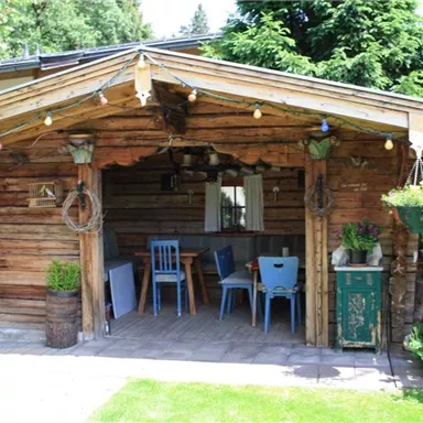 A cozy wooden cabin with rustic charm. The outdoor area is decorated with plants and colorful lights.