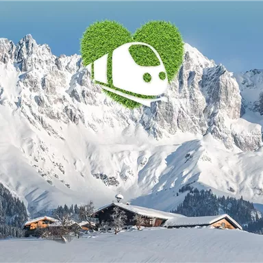 Eine beeindruckende Berglandschaft mit schneebedeckten Gipfeln. Im Vordergrund steht ein traditionelles Haus, umgeben von winterlicher Idylle.