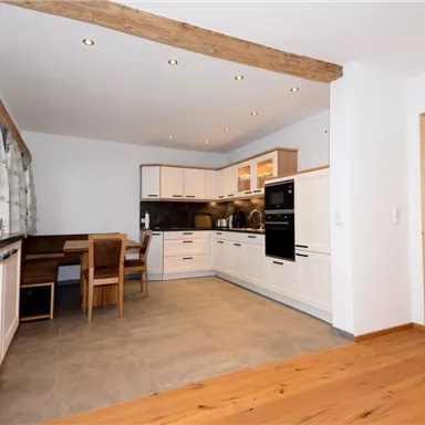 A modern kitchen with bright furniture and wooden details. It features a dining table and a well-equipped cooking area.