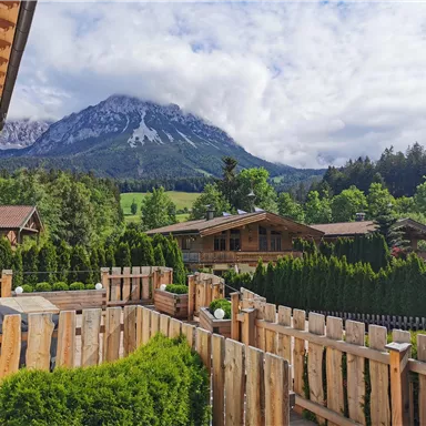 Eine malerische Landschaft mit gut gepflegten Gärten und einem Blick auf majestätische Berge. Die Natur ist grün und einladend, ideal für Erholung und Entspannung.
