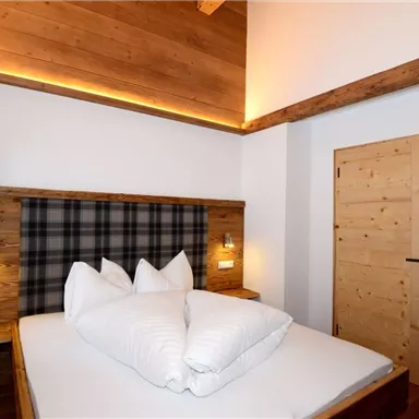 A cozy bedroom with a large bed and wooden paneling. The walls are light and the windows are adorned with green curtains.