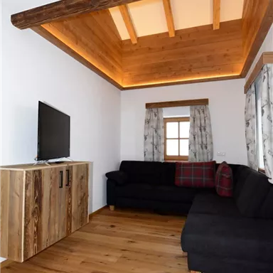 A cozy living space with a black sofa and a wooden table. The wooden ceiling creates a warm atmosphere.