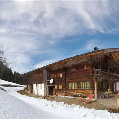 A beautiful wooden house in a snowy landscape. The sky is blue with some clouds.