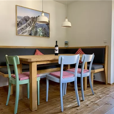 Ein gemütlicher Essbereich mit einem Holztisch und bunten Stühlen. Der Raum hat große Fenster und eine Kose für eine freundliche Atmosphäre.