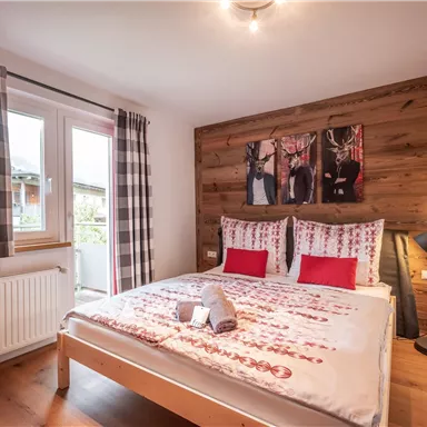 A cozy bedroom with a wooden wall element and two backgrounds with images. The bedding is light and designed with red accents, and the room is well lit.