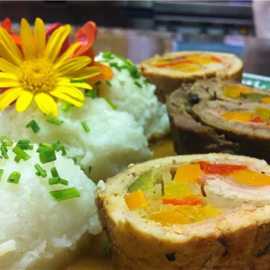 A delicious dish with stuffed meat and colorful vegetables. Served with it are beige rice and a food flower decoration.