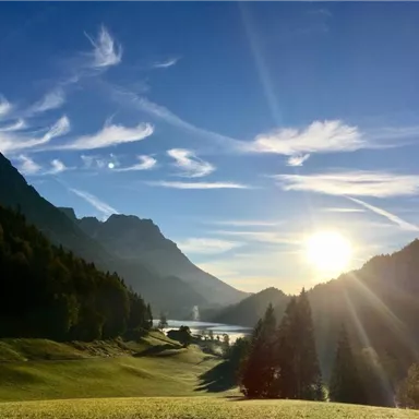 A picturesque landscape with mountains and a clear sky. The sun shines over the gently rolling hills and a lake.
