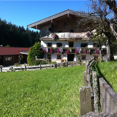 A picturesque country house with flower boxes and a large garden. The surroundings are green and surrounded by trees.