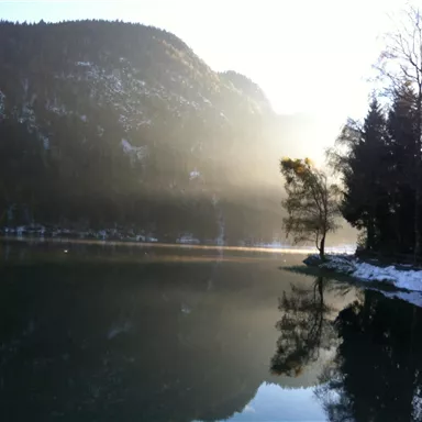 A quiet lake surrounded by mountains and trees. The morning mist creates a mystical atmosphere.