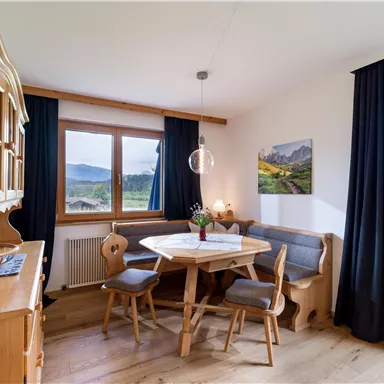 Ein gemütlicher Essbereich mit einem runden Tisch und Holzstühlen. Große Fenster bieten einen Blick auf die Berge und die grüne Landschaft.