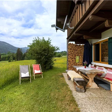 Ein gemütlicher Garten mit einer Holzterrasse und zwei Liegestühlen. Im Hintergrund sind grüne Wiesen und sanfte Hügel zu sehen.