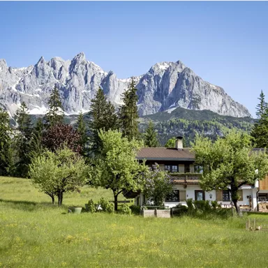 Eine malerische Landschaft mit grünen Wiesen und einer charmanten Unterkunft. Im Hintergrund erheben sich majestätische Berge.