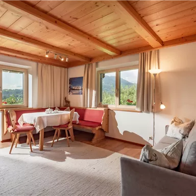 Ein gemütliches Wohnzimmer mit Holzbalkendecke und großen Fenstern. Es gibt ein Sofa, einen Tisch und eine schöne Aussicht auf die Umgebung.