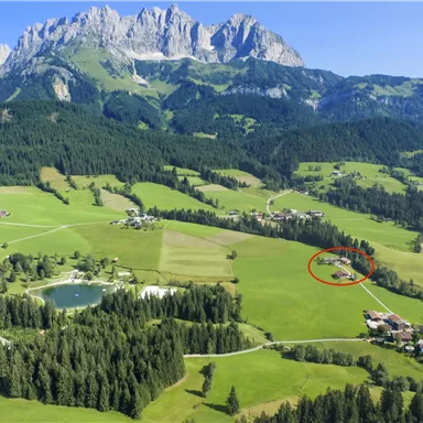 Eine malerische Landschaft mit grünen Wiesen und Bergen im Hintergrund. Ein kleiner Ort ist im unteren Bereich des Bildes sichtbar.