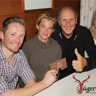 A group of four people is sitting at a table in a cozy room. They all smile and show joy while one of them presents a small gift.