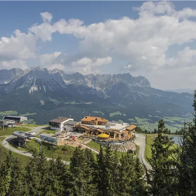 Eine malerische Berglandschaft mit einem modernen Gebäude und Liftanlagen. Die umliegenden Berge sind majestätisch und der Himmel ist teilweise bewölkt.