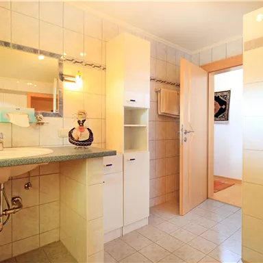 Ein helles Badezimmer mit gefliesten Wänden und einem großen Spiegel. Es gibt eine Dusche und moderne Möbel, die Platz bieten.