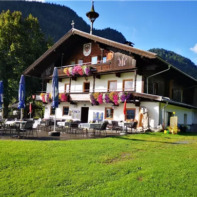 Ein charmantes Landhaus mit bunten Blumen und Sonnenschirmen im Freien. Im Hintergrund sind die grünen Berge zu sehen.