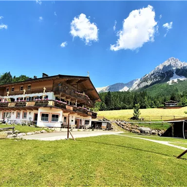 A traditional house in the mountains with a beautiful view. The sky is clear and the surroundings are green and inviting.