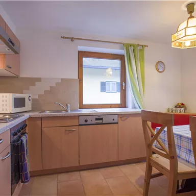 Eine gemütliche Küche mit Holzschränken und modernen Geräten. Ein Esstisch mit Stühlen steht neben einem Fenster mit Blick nach draußen.