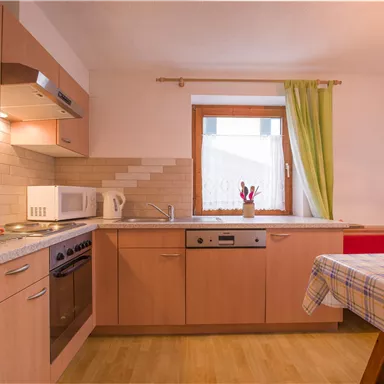 Eine moderne Küche mit Holzschränken und einem großen Fenster. Der Raum ist hell und freundlich, mit einem Tisch und Stühlen.