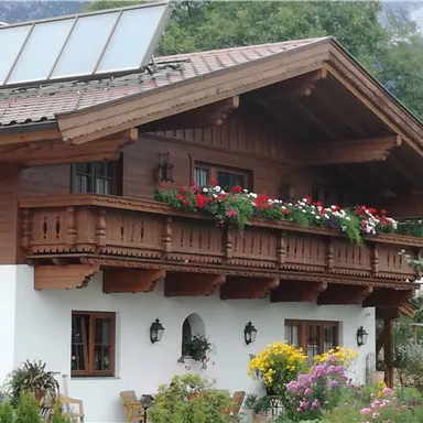 A traditional wooden house with a flower garden and a balcony. Solar panels are installed on the roof.