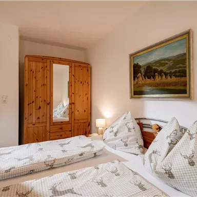 Ein gemütliches Schlafzimmer mit zwei Einzelbetten und rustikaler Holz-Einrichtung. Ein großer Kleiderschrank und ein Bild an der Wand runden das angenehme Ambiente ab.